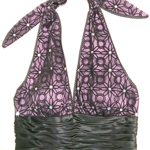 May include: A halter-style dress in shades of purple and black. The bodice features a floral lace overlay with sparkling accents. A black satin band defines the waist, and the halter straps are tied at the back of the neck. Formal wear.