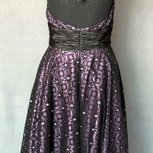 May include: A formal halter dress with a black bodice and a full skirt. The skirt features a floral lace overlay over a lavender fabric, embellished with small, sparkling accents. The dress has a black satin waistband and a matching halter tie.