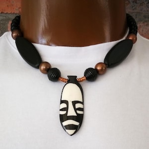 May include: A black and white wooden mask pendant on a necklace with black and copper beads.