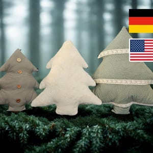 Peut inclure: Trois coussins décoratifs en forme de sapin de Noël, dans des tons de gris et de blanc. L'un est orné de boutons en bois, un autre est uni et le troisième est bordé de dentelle. Les coussins sont présentés sur des aiguilles de pin vertes.