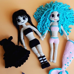 K&ouml;nnte beinhalten: Zwei handgefertigte H&auml;kelpuppen. Eine Puppe hat schwarzes Haar und tr&auml;gt ein schwarz-wei&szlig;es Outfit. Die andere Puppe hat blaues Haar und tr&auml;gt ein rosa-wei&szlig;es Outfit. Ein schwarzes Kleid und eine rosa Meerjungfrauenflosse sind ebenfalls enthalten.