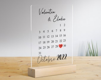 May include: A clear acrylic calendar with a wooden base. The calendar features the names "Valentin & Elodie" and the month of October 2022. The 20th of October is highlighted with a red heart.