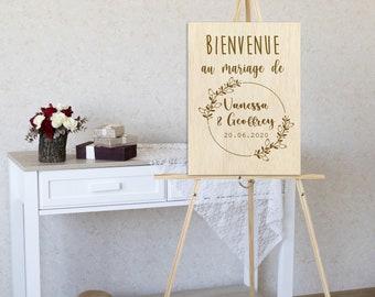 Può includere: Cavallo da cavalletto in legno con un cartello che dice "Bienvenue au mariage de Vanessa & Geoffrey 20.06.2020". Il cartello è decorato con una ghirlanda di fiori.