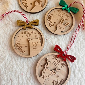 Peut inclure: Quatre décorations de Noël en bois sur le thème des fêtes. Chaque décoration présente un animal différent, notamment un pingouin, un lapin, un ours polaire et un renne. Les décorations sont personnalisées avec des noms et l'année 2023.