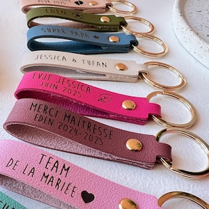 Peut inclure: Un ensemble de dix porte-clés en cuir colorés avec des anneaux dorés. Chaque porte-clés porte une inscription différente, notamment "Future Mamie", "Super Papa", "Team de la Mariée" et "Future Marraine".