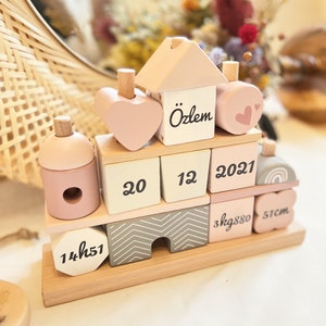 Peut inclure: Un ensemble de blocs de construction en bois de couleur rose et blanche. Les blocs présentent une maison, un cœur et des chiffres. Les blocs comprennent également le nom "Ozlem", la date "2021" et les mesures "3kg880" et "51cm".