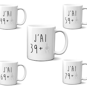 Peut inclure: Ensemble de cinq tasses en céramique blanche avec du texte noir et un dessin simple au trait d'un majeur. Les tasses présentent le texte "J'AI" suivi d'un nombre et d'un signe plus. Les nombres sont 39, 49, 59, 69 et 79.