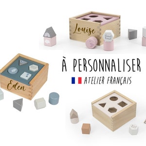 Peut inclure: Deux boîtes en bois de tri de formes avec des formes de différentes couleurs et un nom personnalisé sur le devant. Les boîtes sont en bois naturel et ont une finition brun clair. Les formes sont en bois peint et ont différentes couleurs et motifs. Les boîtes sont un excellent moyen pour les enfants d'apprendre les formes et les couleurs.