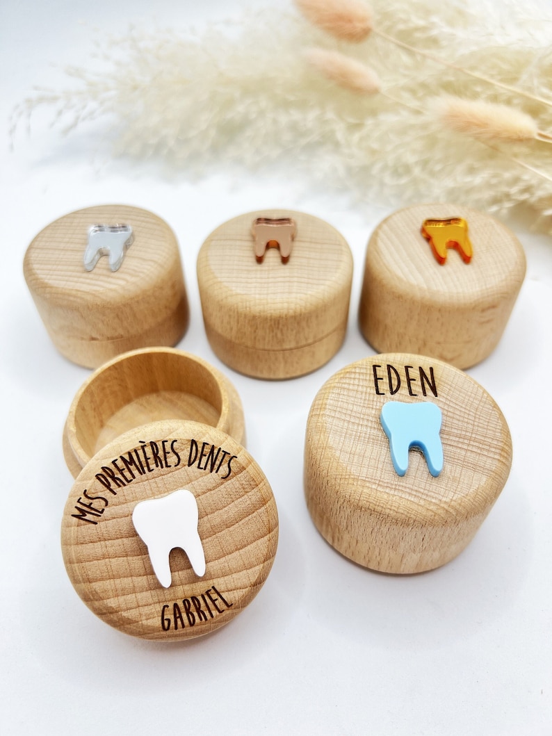 May include: Four wooden boxes with lids, each decorated with a tooth-shaped design and a name. The boxes are for storing baby teeth. The names on the boxes are Eden, Gabriel, and two other names that are not visible.
