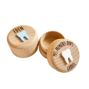 May include: Two wooden boxes with lids for storing baby teeth. The box on the left has a blue tooth on the lid and the text "EDEN". The box on the right has a white tooth on the lid and the text "MES PREMIERES DENTS GABRIEL".