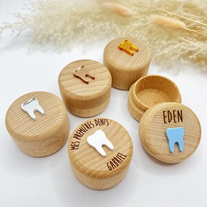 May include: Four wooden boxes with lids for storing baby teeth. Each box has a different coloured tooth charm and is personalised with a name. The boxes are on a white surface with dried pampas grass.