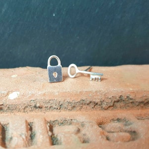 May include: A pair of silver earrings, one shaped like a padlock and the other shaped like a key.