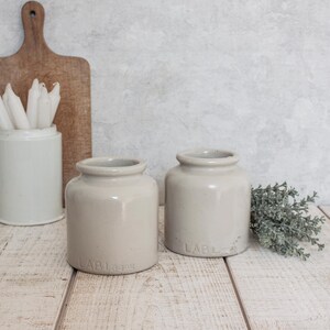Peut inclure: Deux pots en grès vintage avec un glaçage gris clair. Les pots ont un corps arrondi et une large ouverture. Les pots sont étiquetés "LABL" et "LABL 399".
