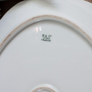 May include: White porcelain serving dish with a scalloped edge. The underside features the text "B & C&deg; LIMOGES FRANCE" in black lettering. The dish has a smooth, glossy surface and a slightly off-white hue.