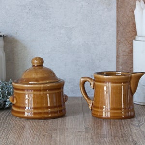 Peut inclure: Un sucrier en céramique marron avec un couvercle et un pot à crème assorti en céramique marron.