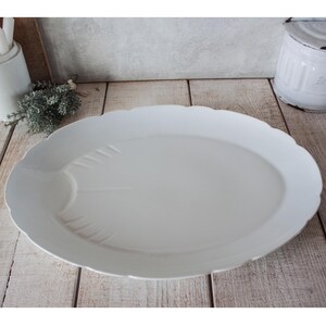 May include: A large, white, oval serving platter with a scalloped edge. The platter has a smooth surface with subtle embossed details. The design is simple and elegant, suitable for serving a variety of dishes. The platter is made of ceramic.