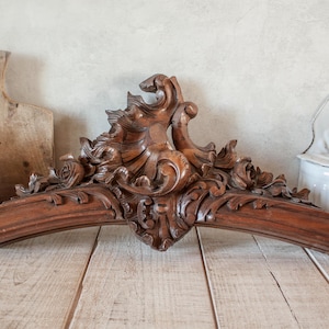 Könnte beinhalten: Antikes Holzmöbelornament mit aufwendigen floralen und scrollartigen Schnitzereien. Das braune, gebogene Stück ist wahrscheinlich ein dekoratives Element, möglicherweise von einem Spiegel oder einem Kopfteil.