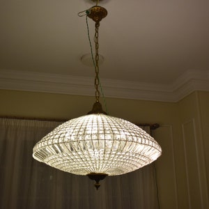 May include: A crystal chandelier with a gold finish and a clear glass shade. The chandelier is hanging from the ceiling and is illuminated.