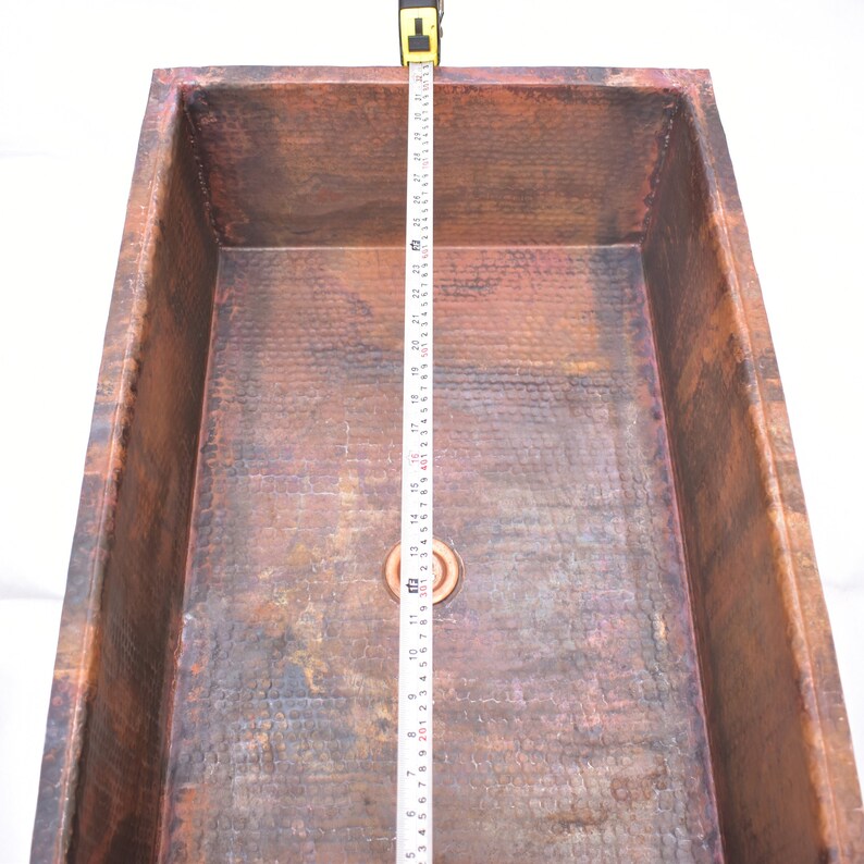 May include: A rectangular copper sink with a hammered finish. The sink is 29 inches long and has a drain in the center.