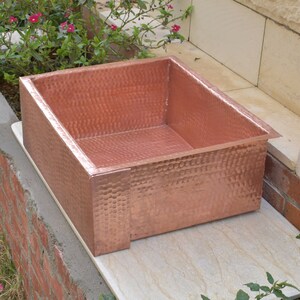 May include: A hammered copper sink with a square shape. The sink is made of solid copper and has a rustic, hand-crafted look.
