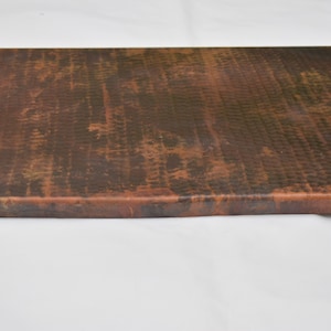 May include: A close-up of a copper countertop with a hammered finish. The copper has a dark patina and shows signs of age.