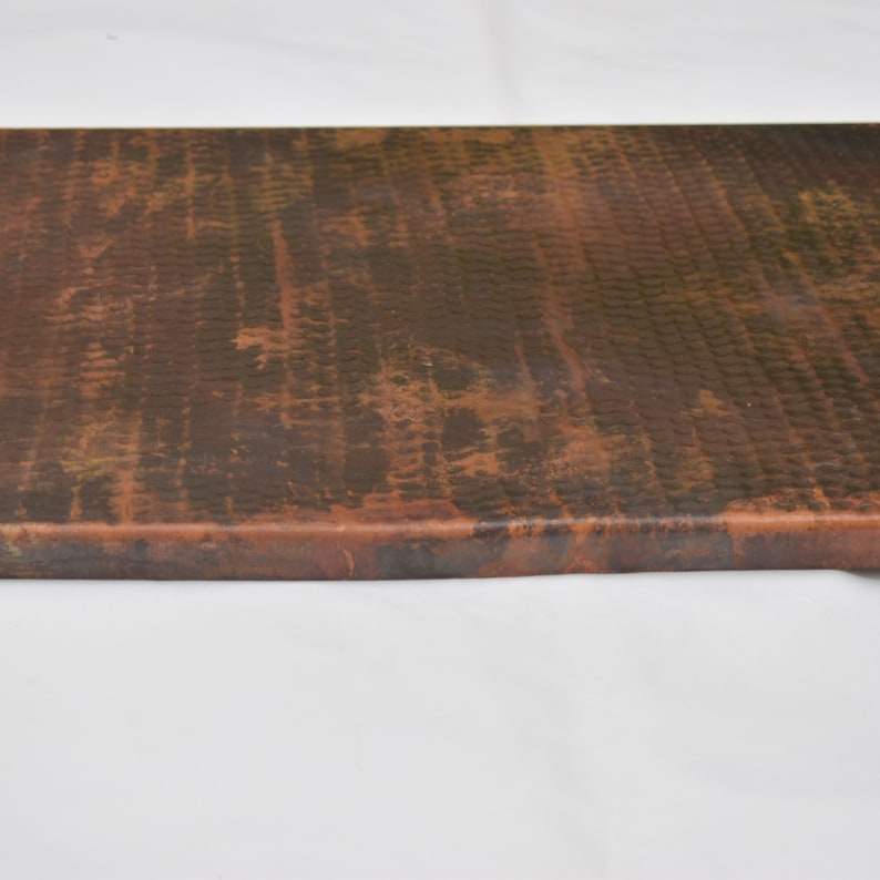 May include: A close-up of a copper countertop with a hammered finish. The copper has a dark patina and shows signs of age.