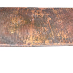 May include: A hammered copper countertop with a rustic, aged finish. The surface has a textured, hammered look with variations in color, including shades of brown, gold, and green.