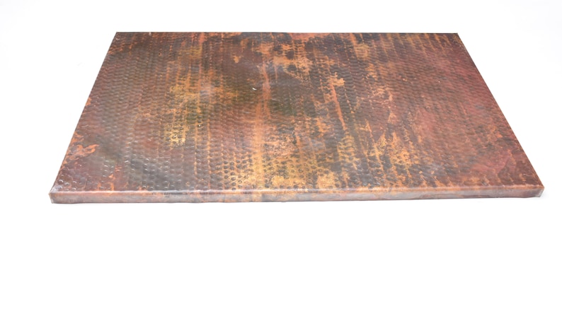 May include: A hammered copper countertop with a rustic, aged finish. The surface has a textured, hammered look with variations in color, including shades of brown, gold, and green.