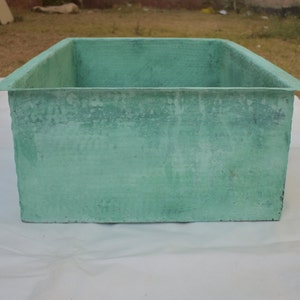 May include: A large, rectangular, green concrete planter. The planter has a rough, textured surface.
