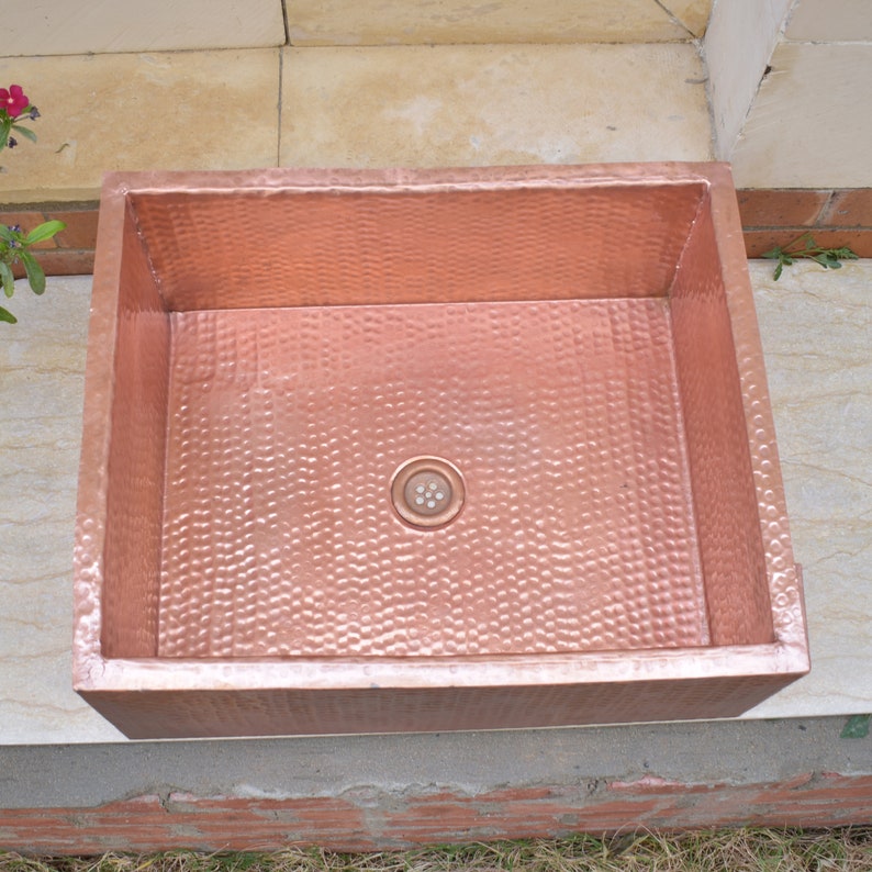 May include: A rectangular copper sink with a hammered finish. The sink has a drain hole in the center.