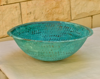 May include: A large, teal-coloured copper bowl with a hammered texture. The bowl is round and has a wide, shallow opening.