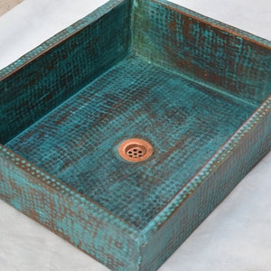 May include: A rectangular copper sink with a hammered finish and a turquoise patina. The sink has a single drain hole in the center.