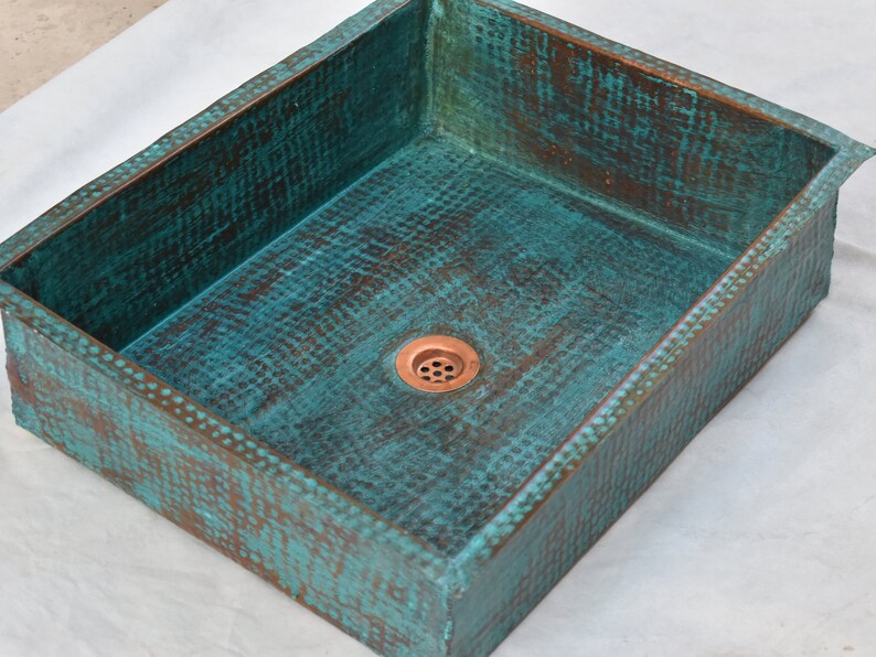 May include: A rectangular copper sink with a hammered finish and a turquoise patina. The sink has a single drain hole in the center.