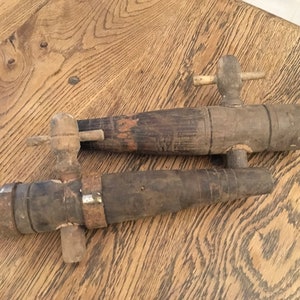 Op de afbeelding: Twee houten vatenkraantjes met een metalen band op een. De kraantjes liggen op een houten oppervlak.