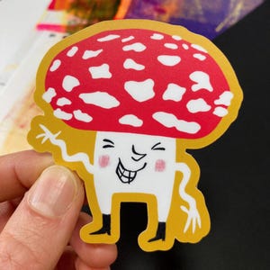 May include: A red and white mushroom with a smiling face and yellow background. The mushroom has a white stem and black eyes.