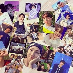 May include: A collection of rectangular photo cards featuring various individuals in diverse poses and settings. The cards display a range of colors, including blues, greens, and purples, with some cards showing text. The cards are scattered across a light-colored surface.