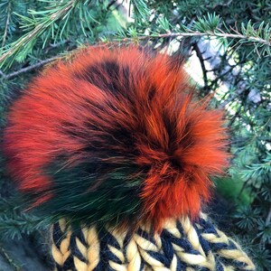 May include: A black, green, and orange knit hat with a fluffy pom pom.