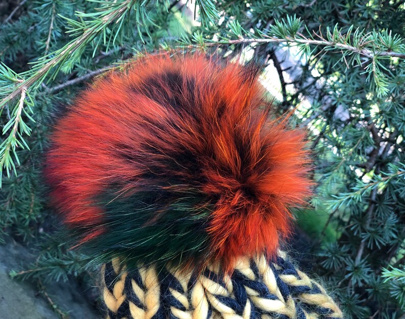 May include: A black, green, and orange knit hat with a fluffy pom pom.