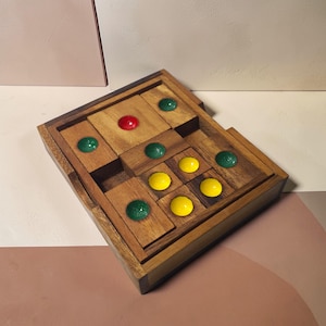 Peut inclure: Un jeu de puzzle en bois avec un design de blocs coulissants. Le jeu comprend un cadre en bois avec divers blocs de bois et des chevilles colorées, rondes, rouges, vertes et jaunes. Le puzzle est conçu pour être résolu en faisant glisser les blocs.