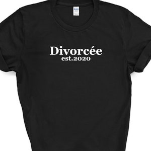 May include: Black t-shirt with the white text "Divorc&eacute;e est.2020". The shirt has rolled-up sleeves and a crew neck. The Gildan brand tag is visible on the upper back of the shirt.