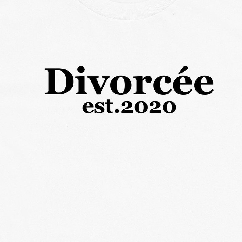 May include: White t-shirt with the word "Divorc&eacute;e" in bold black font above "est.2020". The text is centered on the shirt, creating a simple yet impactful design.