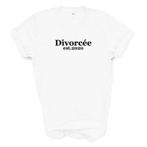 May include: White t-shirt with the word "Divorc&eacute;e" in a bold, black font, with "est.2020" below it. The shirt has rolled-up sleeves and a crew neck. The background is plain white.