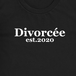 May include: Black t-shirt with the white text "Divorc&eacute;e est.2020" printed across the front. The text is in a bold, sans-serif font. The shirt has a crew neck.