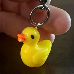 May include: A yellow rubber ducky keychain with an orange beak and black eyes. The ducky is attached to a silver key ring.