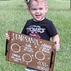 May include: A wooden tray with the words "Dear Santa" and a list of items for Santa to bring: cookies, milk, and carrots for the reindeer. The tray is decorated with stars and hearts. The text "Love Memphis" is written at the bottom of the tray.