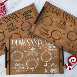 May include: Three wooden trays with black handles, each with the text "Dear Santa" and a space for milk, cookies, and carrots for the reindeer. The trays are decorated with stars and hearts. The text "Love" is written on each tray, followed by a name.