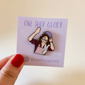 May include: Purple and white enamel pin featuring a cartoon illustration of a woman wearing a purple hat and a pink apron. The woman's face is covered by a white rectangle with the text "I'm breaking down" written on it. The pin is on a purple card with the text "One Shop Glory" and the social media handle "@oneshopglory".