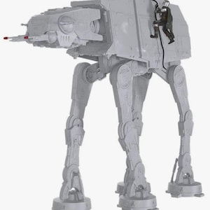 May include: A light gray plastic AT-AT walker toy featuring a four-legged design with a head-mounted cannon. A small, detailed figure in dark armor is attached to the side of the walker, connected by a black cable, showcasing intricate mechanical details.
