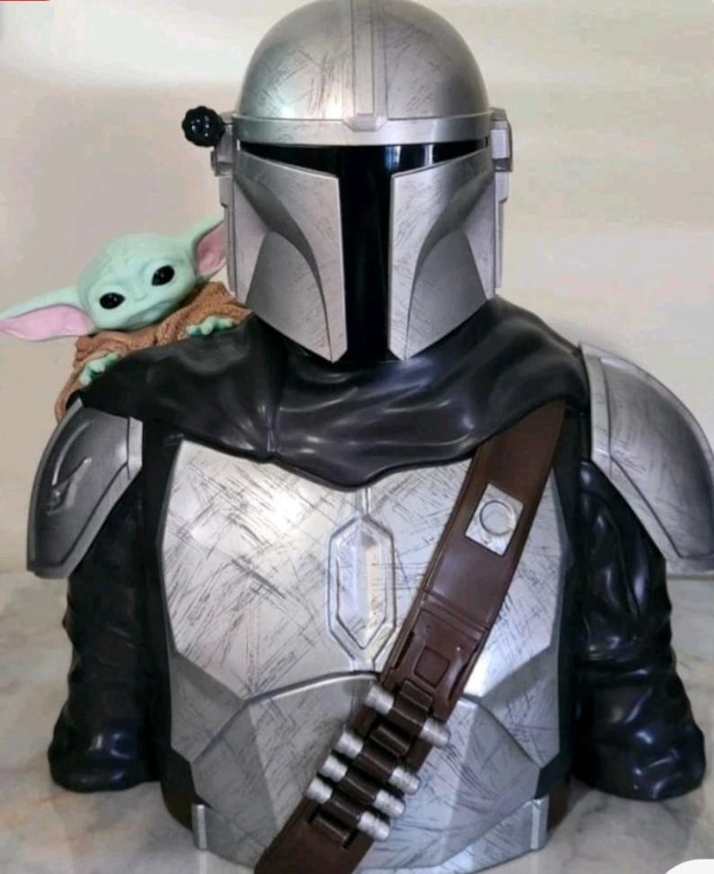 K&ouml;nnte beinhalten: Eine B&uuml;ste einer silbernen R&uuml;stungsfigur mit Helm und schwarzem Visier, die ein verwittertes Metallic-Finish aufweist. Eine kleine gr&uuml;ne Kreatur mit gro&szlig;en Ohren und einem beigen Gewand sitzt auf der Schulter der gepanzerten Figur.