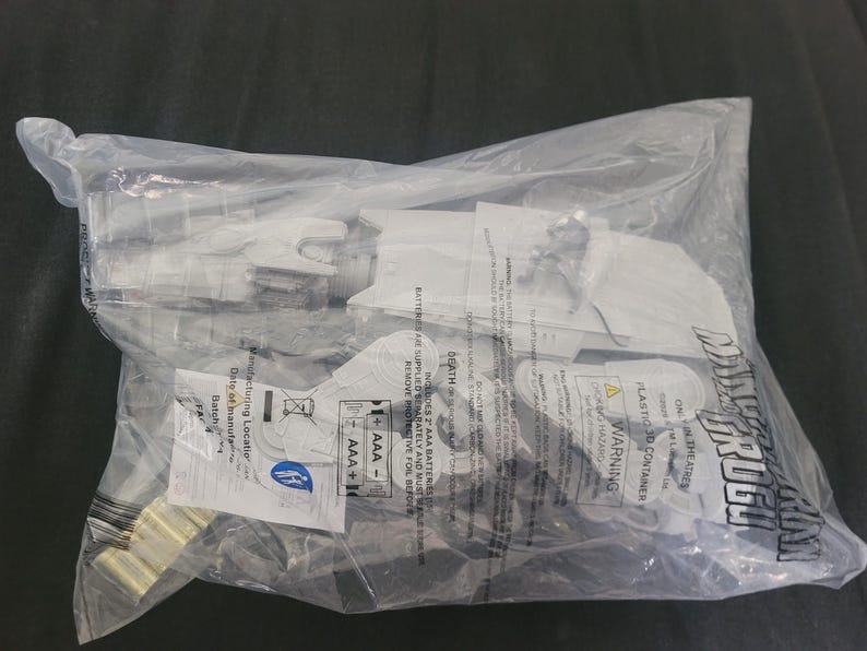 May include: A white plastic Star Wars The Mandalorian Grogu toy set sealed in a clear plastic bag. The packaging features black text including the title, warning labels, and battery requirements for two AAA batteries. The toy includes a figure.